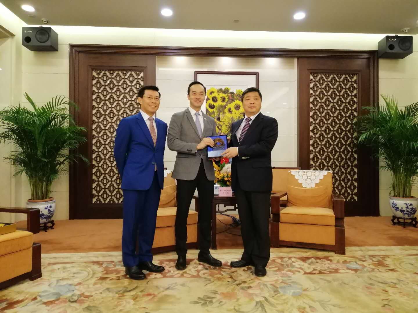 Three men in suits pose in a room with CAV speakers, sunflower art, and patterned decor.